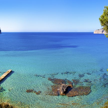 Uitzicht over zee met bomen, rotsen en een boot op Mallorca