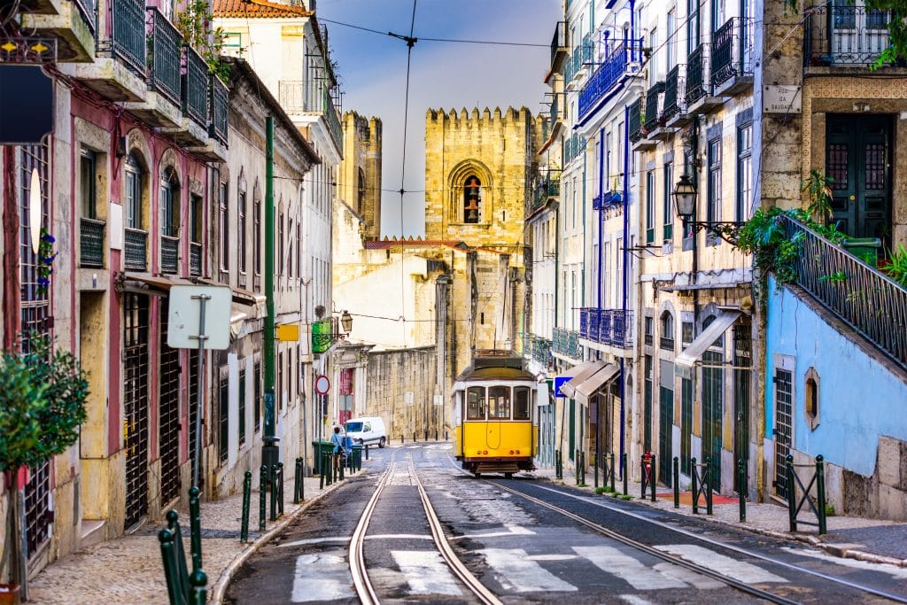 tram toren huizen lissabon portugal Tram tussen huizen met toren op de achtergrond in Lissabon, Portugal