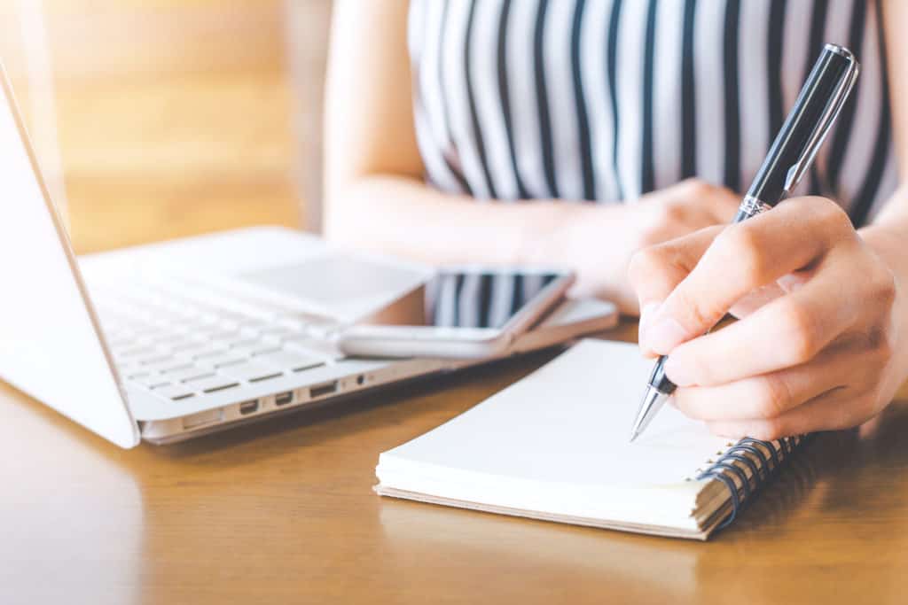 vrouw schrijft met pen kladblok bij haar laptop telefoon Vrouw schrijft met pen op een kladblok bij haar laptop en telefoon
